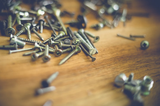 different types and sizes of nails and screws on a wooden table