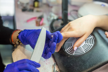 Manicurist with blue gloves rasping nails on women's hand in nail salon.