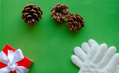 Christmas flat lay with white mittens and a gift in a red wrapper and Xmas  pine cones on green background. Winter holiday. Happy New Year. 