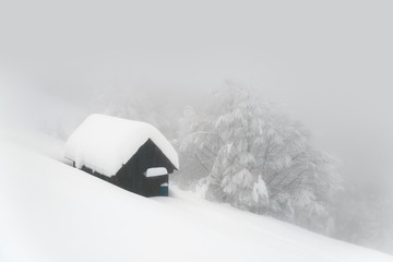 Minimalistic winter landscape with wooden house in snowy mountains. Cloudy weater, landscape photography