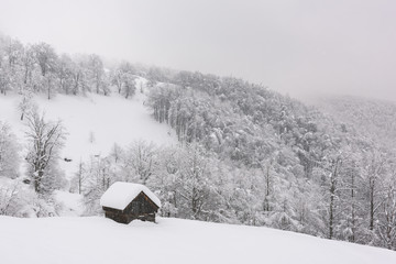 Minimalistic winter landscape with wooden house in snowy mountains. Cloudy weater, landscape photography