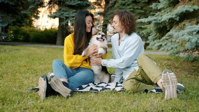 Slow motion of man and woman loving couple kissing corgi dog sitting on lawn in park enjoying leisure time outdoors. Lifestyle and domestic animals concept.