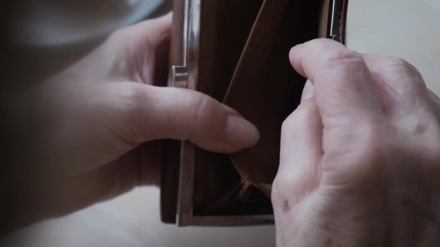 Empty wallet in the wrinkled hands of an unhappy old woman, close-up
