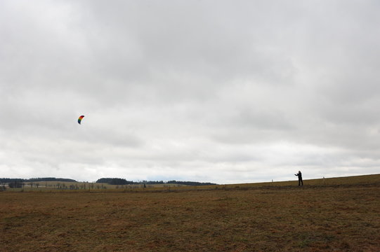 Young woman in the field playing with a kite in the clouds on windy and foggy autumn afternoon. Czech countryside.