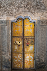 The old yellow two-fold doors with drawings on religious subject conducting in one of Buddhist...
