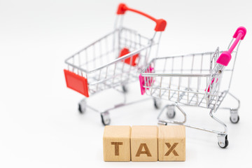 Tax letter on wooden block with coins stack, shopping cart and home model on white background.