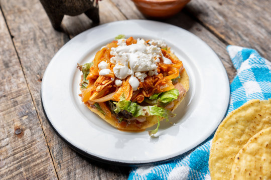 Mexican chicken tinga toasts with chipotle pepper and fresh cheese also called "tostadas" on wooden background