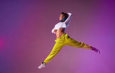 Tuinposter Charming young lady jumping high making acrobatics movies in the air, performing dancing skills, isolated on bright coloured background, urban lifestyle concept © alfa27