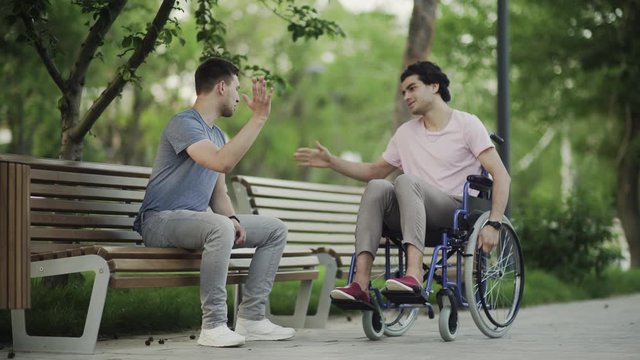 Young man in a wheelchair meet his friend in the park.