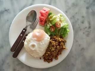 Thai food - Spicy stirred fried pork chop served with rice, fried egg, and vegetables on a white...