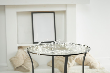 Round glass table with some winter ornaments and decoration with bright white fireplace wall background. Christmas time. Nice luxurious home interior.