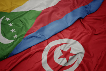 waving colorful flag of tunisia and national flag of comoros.