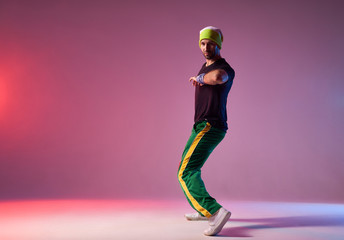 Fototapeta na wymiar Modern breakdancer in sportive clothes, stretching elbow towards camera, looking away with brutal face, demonstrating dancing skill, posing on pink background
