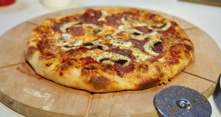 Selbstgemachte Pizza auf Holzbrett mit Salami und Pilzen lecker