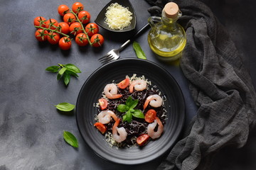 Squid Ink Pasta with seafood, parmesan, basil leaves, cherry tomatoes. Black spaghetti, black organic noodles with shrimps. Mediterranean gourmet food.