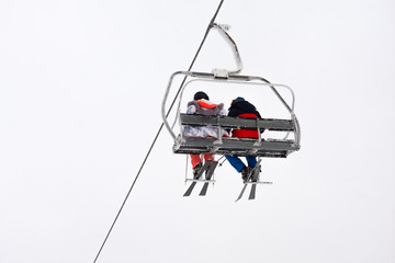 Pareja de esquiadores sentados en telesilla bajo un cielo completamente blanco
