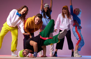 Professional hip hop dancer in motion, leaning on hands, standing upside down, showing break dance for people surrounding dancer, performance in brightly lighted studi
