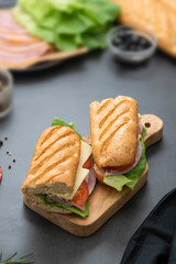 Sandwich with baguette bread, ham, lettuce, tomatoe over dark background. Breakfast or fast food.