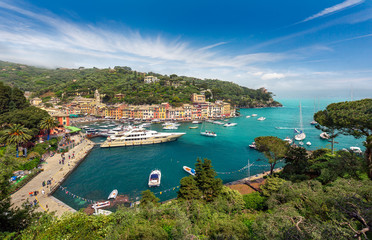 Fototapeta premium Portofino, Riwiera Włoska, Liguria, Włochy - Panorama kolorowej nadmorskiej miejscowości z pięknym niebem i wielokolorowymi domami, willami, luksusowymi jachtami i łodziami rybackimi w turkusowej zatoce portowej