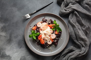 Squid Ink Pasta with seafood, parmesan, basil leaves, cherry tomatoes. Black spaghetti, black organic noodles with shrimps. Mediterranean gourmet food.