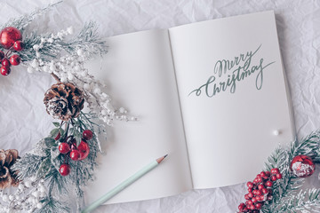 Christmas concept. White notebook with christmas decoration, wreath on a white background. Minimal winter vacation idea. Flat lay top view composition.
