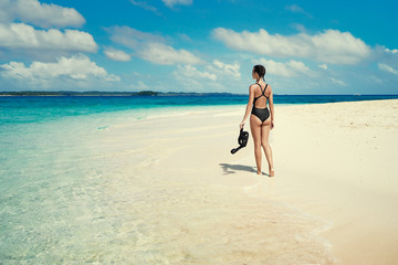 Fototapeta na wymiar Tropical vacation. Young woman walking on tropical blue sea beach with snorkeling gear at sunny day.