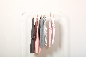 Fashionable clothes on hangers on a wardrobe rack on a light background.
