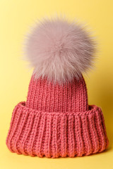 Obraz na płótnie Canvas Close-up knitted hat with fur on yellow background. Top view. Flat lay. Outfit for cold weather. Comfortable autumn, winter clothes. Trendy colors concept