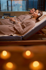 Young caucasian couple relax on loungers in spa center, taking rest together, lying around candles