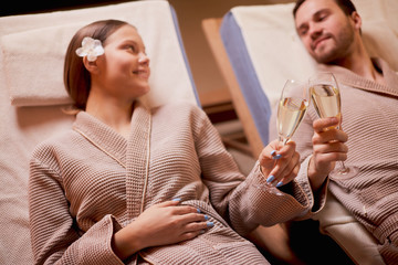 Spa, relax, enjoying concept. Married couple together relaxing in spa salon, lying on beds drinking champagne, using candles