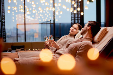 Young caucasian couple take care of body together lying in spa salon and drinking champagne,...