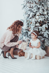Merry Christmas Mom and Daughter Exchanging Gifts. Happy Winter Holiday. Cheerful Woman give Little Girl Present. Parent and Adorable Child Fun near New Year Tree Indoors. Loving Family