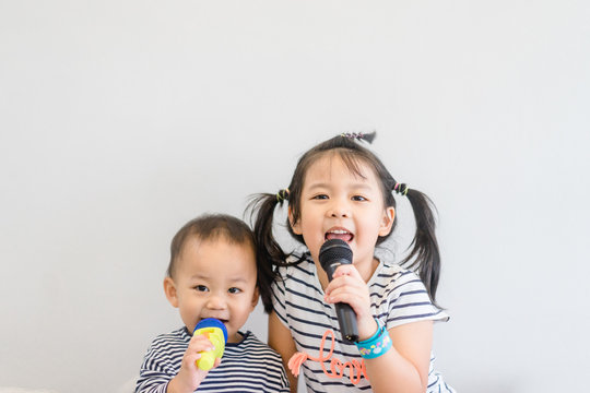 Little sister and her baby brother holding microphone and singing at art music school.Cute girl and baby boy relax learn to sing in music song class.Family with children and Art Education for Child.