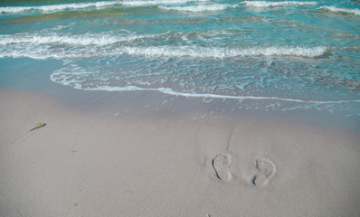 Footprints in the sand on the beach, partially washed by the sea waves. Holiday on the beach with white sand and blue sea.