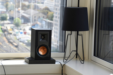 A modern living room interior with high quality speaker and lamp at the corner in front of the windows during daylight