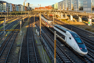 Modern commuter train on a European railway station at sunrise with rail tracks and trains