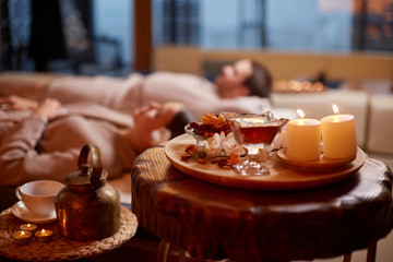 young caucasian man and woman wearing bathrobe, lying down and relxing at spa in beauty salon.Closeup photo of tea and candles while couple lying behind. Relax and healthy lifestyle concept