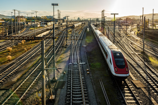 Modern commuter train on a European railway station at sunrise with rail tracks and trains