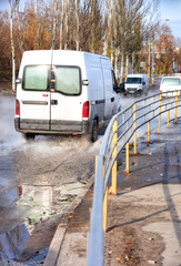 Trucks drive along a road filled with hot water, after breaking through the city heating main, a metal fence separates the carriageway from the sidewalk.