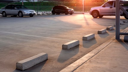 Concrete wheel stops with empty space and three cars parked in outdoor parking lot area with flare...