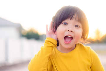 Little asian girl holds her hand near her ear and listening something.Exciting face on funny child...