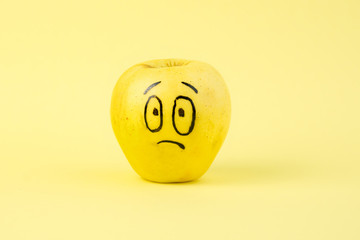 sad Face on an apple - abstract image of human emotions on a yellow background
