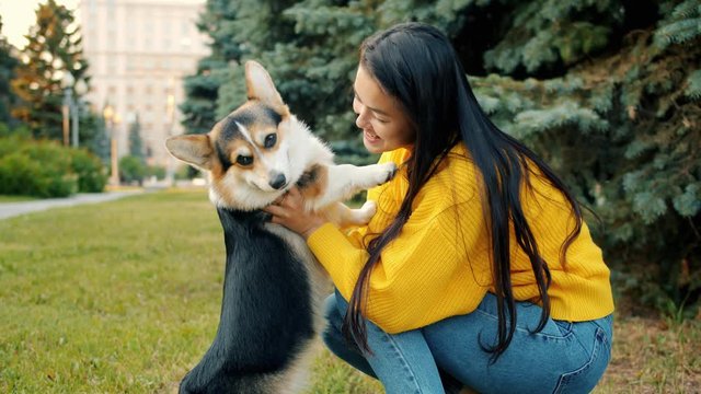 Slow motion of Asian girl hugging and kissing cute corgi dog outdoors in city park expressing love and tenderness. People, animals and nature concept.