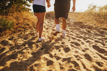 Couple man and woman in sneakers walking on the sand. Close up shoot of legs