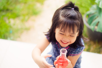 Happy Little scientist asian girl with red liquid into flask and shaking on white background.Home school girl learning about science and pouring reagent into flask.Chemistry class at home.