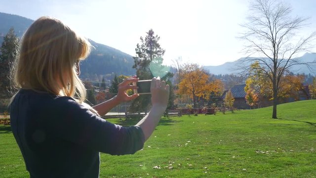 Female Taking Pictures With Smart Device In The Park With Mountains