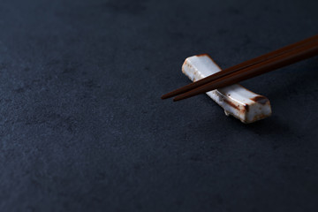 Wooden chopsticks and chopstick rest on dark stone background. Close up. Copy space. 