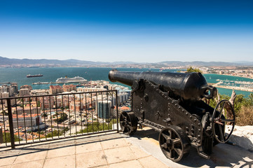 Gibraltar, monkey rock, a berber monkey sitting on a railing, behind it the sea gorge of Gibraltar with airport. UK