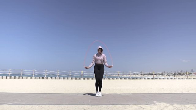 beautiful young leggy fit woman jumping with feints on a skipping rope near the beach along the sea. wide shot