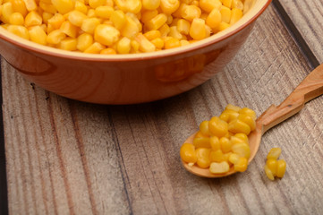 Sweet corn kernels in a plate and on a wooden spoon on a wooden table. Fitness diet. Healthy diet. For a sweet treat. Close up.
